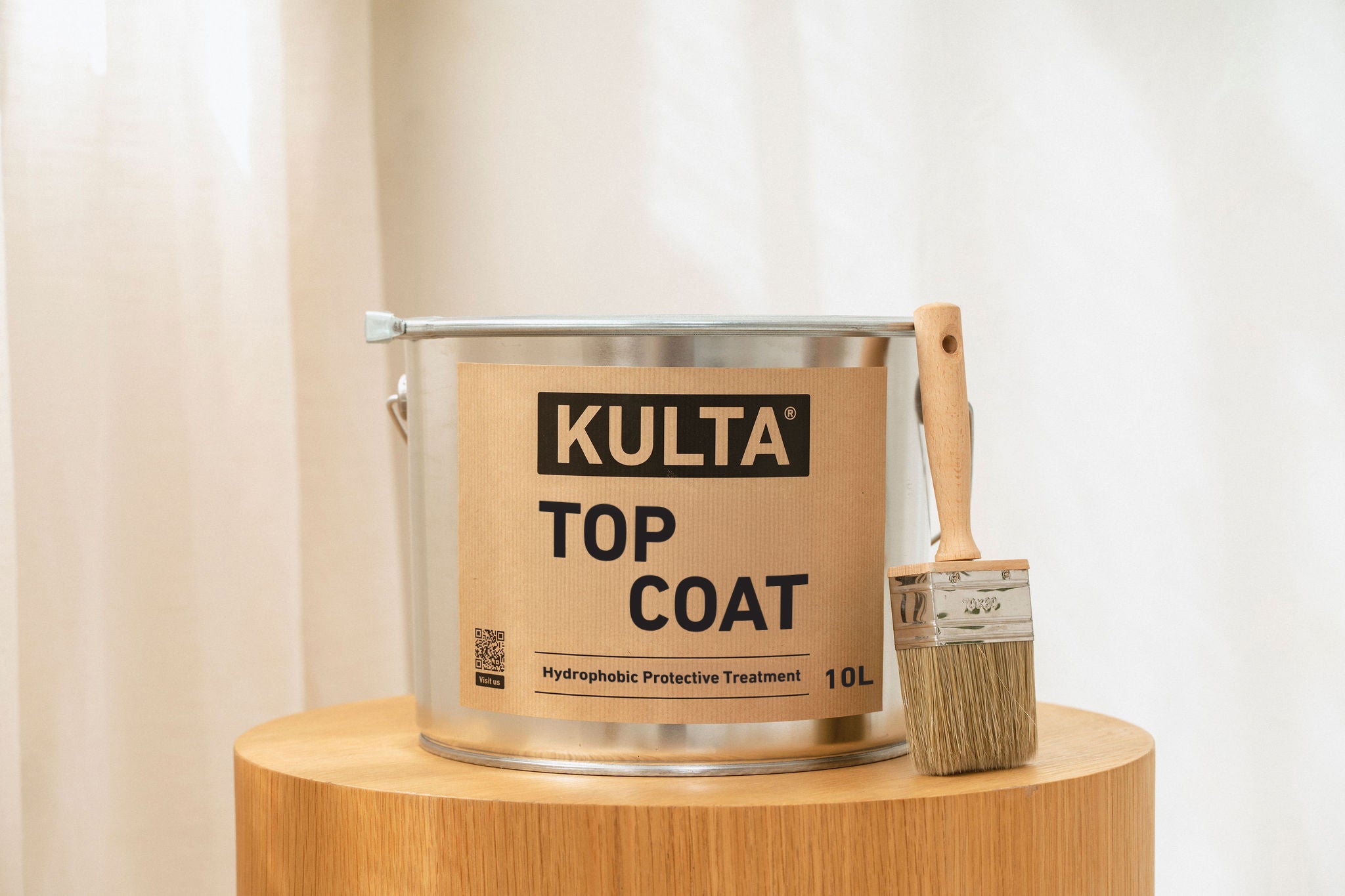 Kulta top coat paint bucket with a brush on a wooden stand against a white curtain background